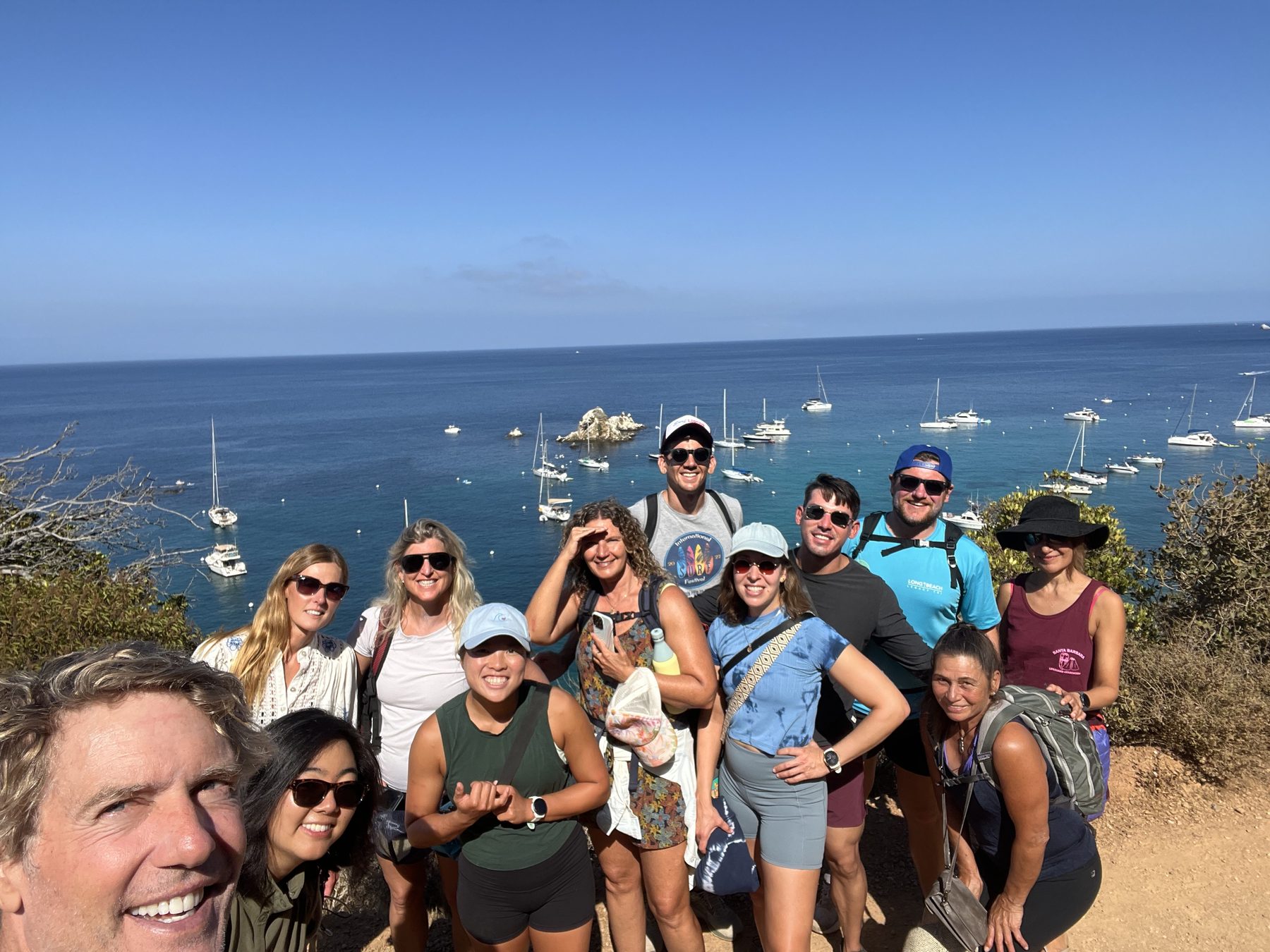 A group looking out over Catalina's anchorage from a coastal trail, boats moored in the water below