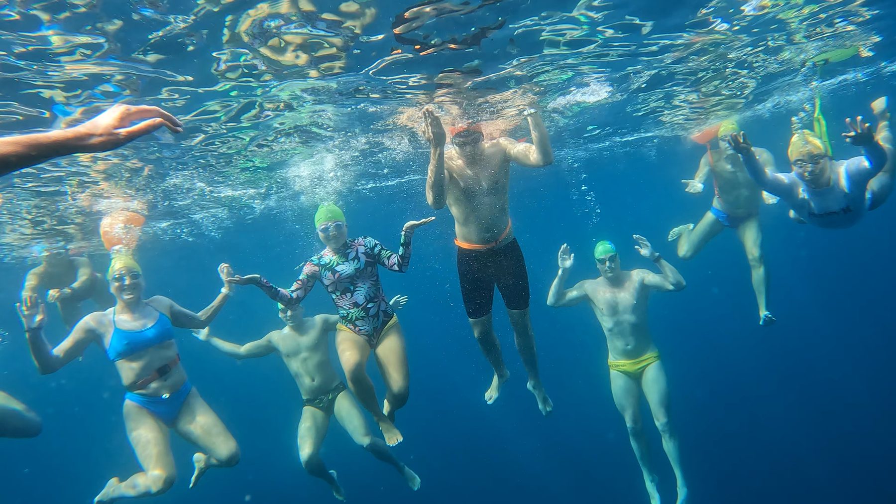 Swimmers linked hand to hand underwater, sunlight above them